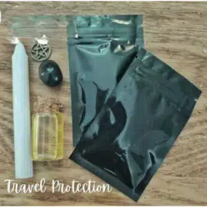 Travel Protection Spell Kit featuring a white candle, black tourmaline crystal, pentagram charm, protection oil, and two black foil herbal sachets on a wooden surface.